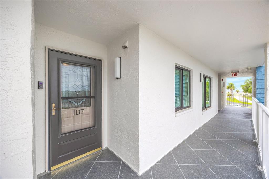 An exterior view of a residential unit entrance with a gray door and tiled walkway — 4620 BAY BOULEVARD UNIT 1117, PORT RICHEY, FL