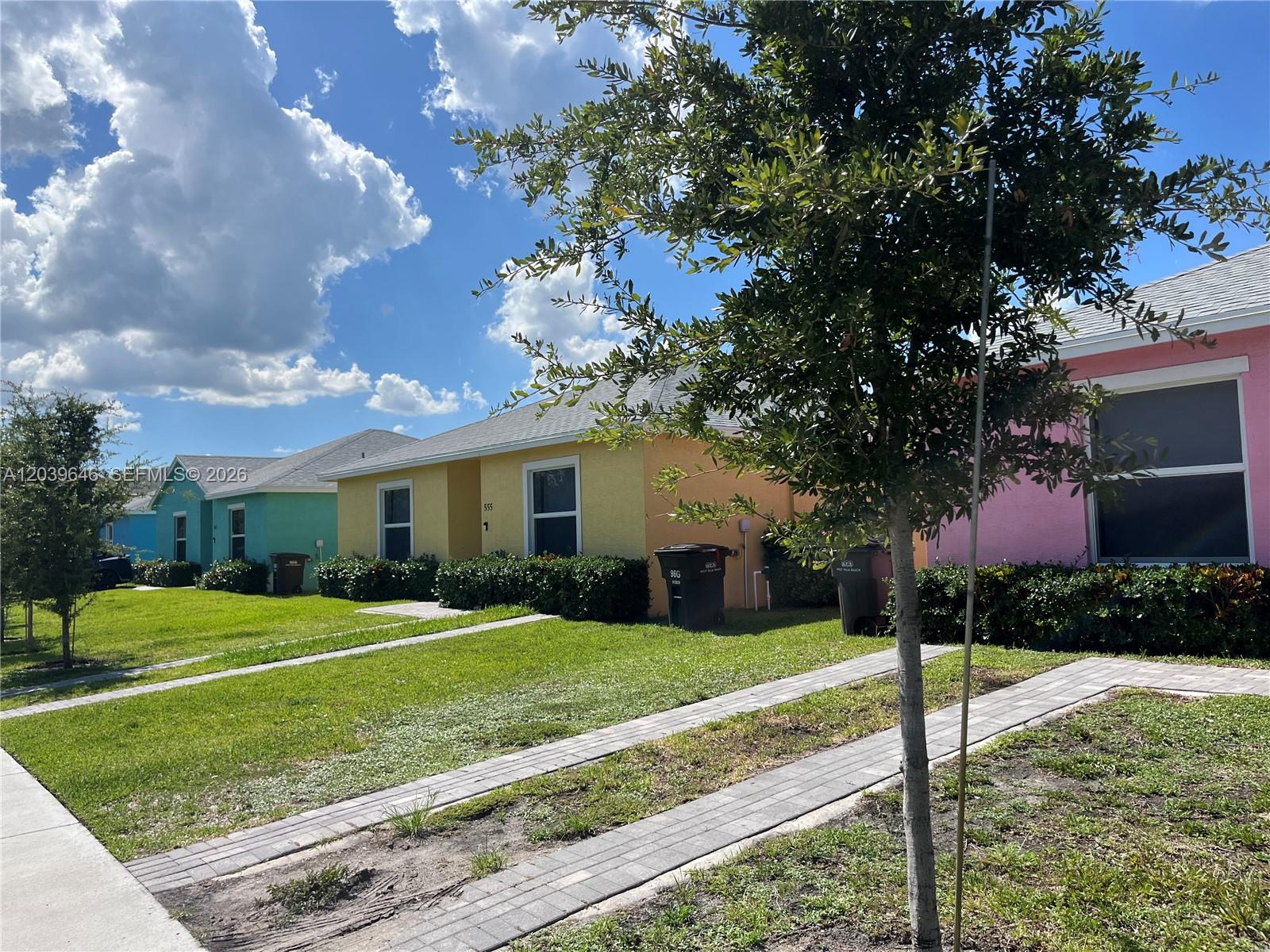 A row of colorful single-story houses features paved driveways and green lawns under a blue sky — 535 Lilac CT, West Palm Beach FL 33407, WEST PALM BEACH, FL