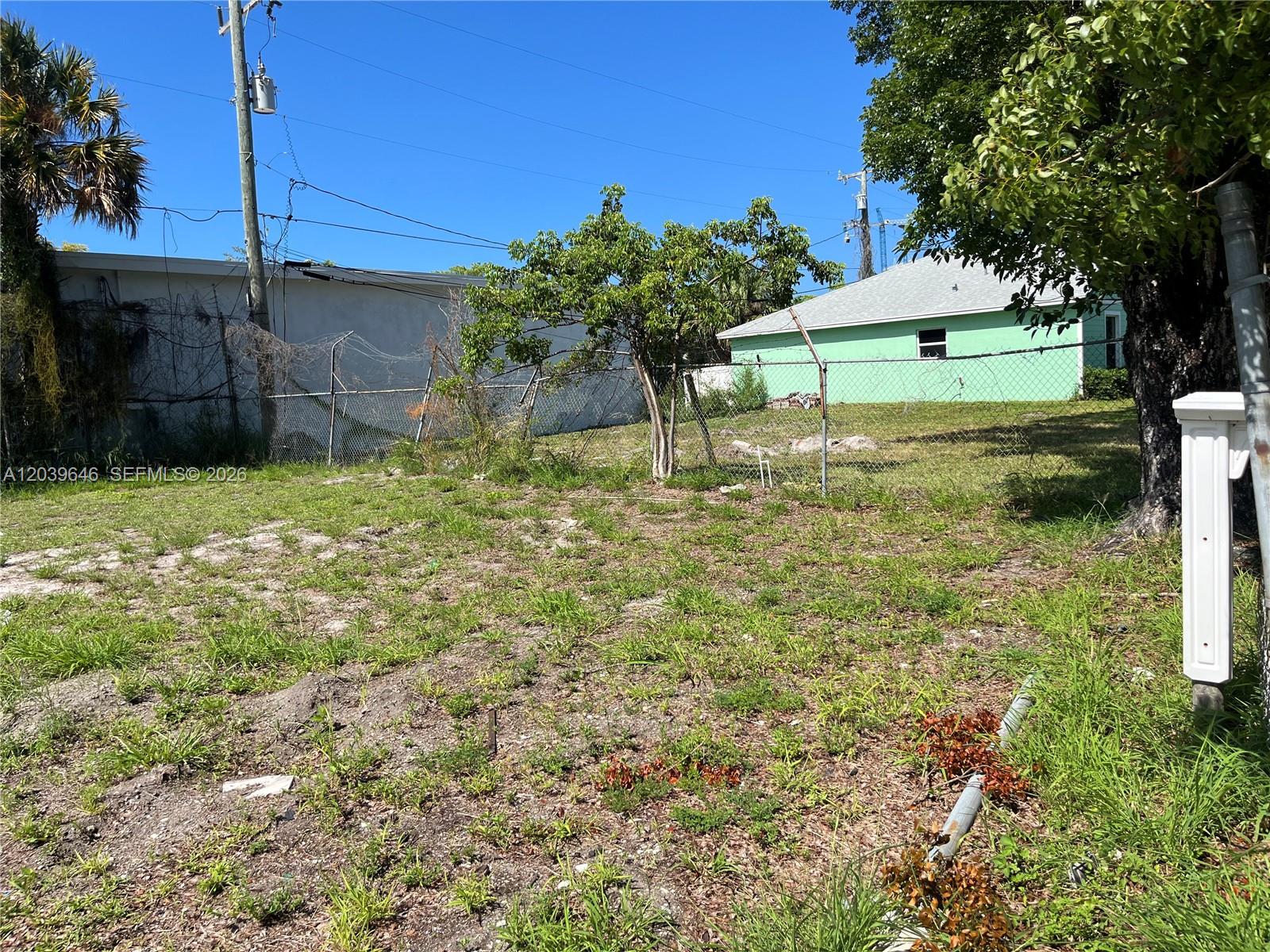 A grassy, fenced-in vacant lot features a small tree and a nearby green house — 535 Lilac CT, West Palm Beach FL 33407, WEST PALM BEACH, FL