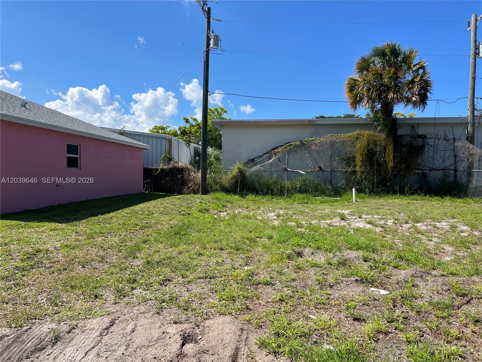 A grassy vacant lot sits between a pink building and a fenced-in structure — 535 Lilac CT, West Palm Beach FL 33407, WEST PALM BEACH, FL
