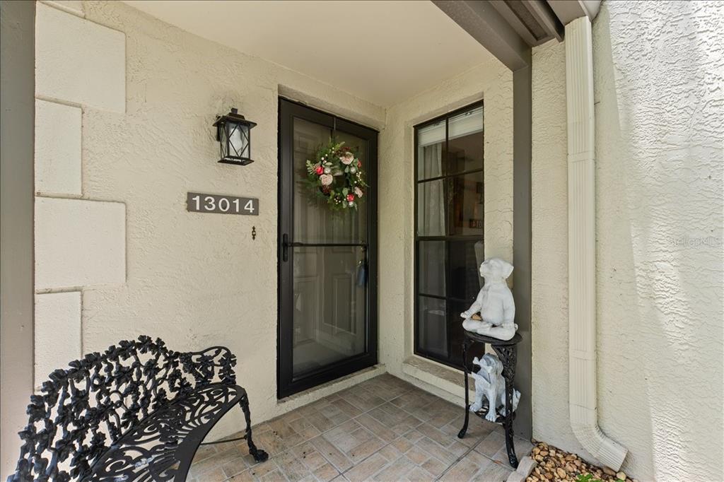 A covered entryway features a black storm door, a metal bench, and a decorative statue — 13014 VILLAGE CHASE CIRCLE, TAMPA, FL