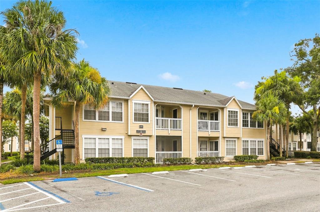 A two-story apartment building with tan siding, screened balconies, and a parking lot in front — 1085 S HIAWASSEE ROAD UNIT 523, ORLANDO, FL