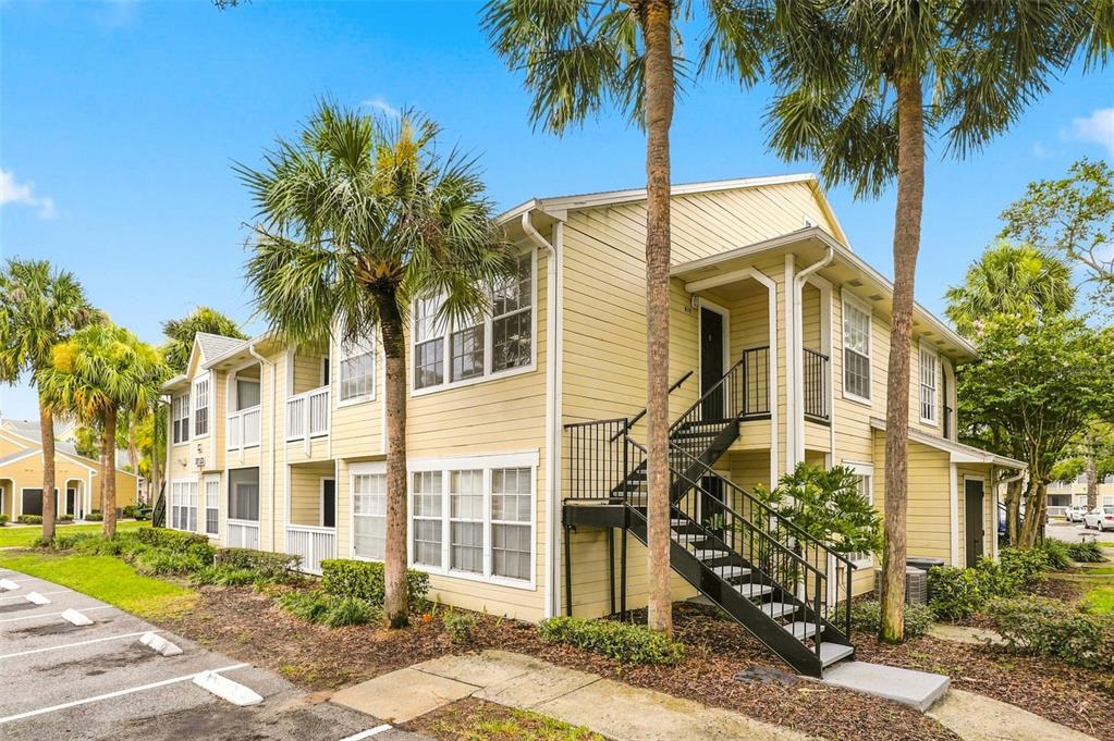 A two-story yellow apartment building features an exterior metal staircase and surrounding palm trees — 1085 S HIAWASSEE ROAD UNIT 523, ORLANDO, FL