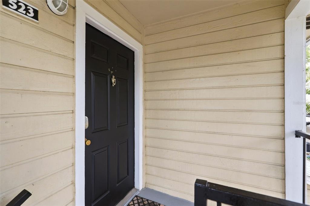 A black front door with a brass knocker is set into light-colored horizontal siding — 1085 S HIAWASSEE ROAD UNIT 523, ORLANDO, FL