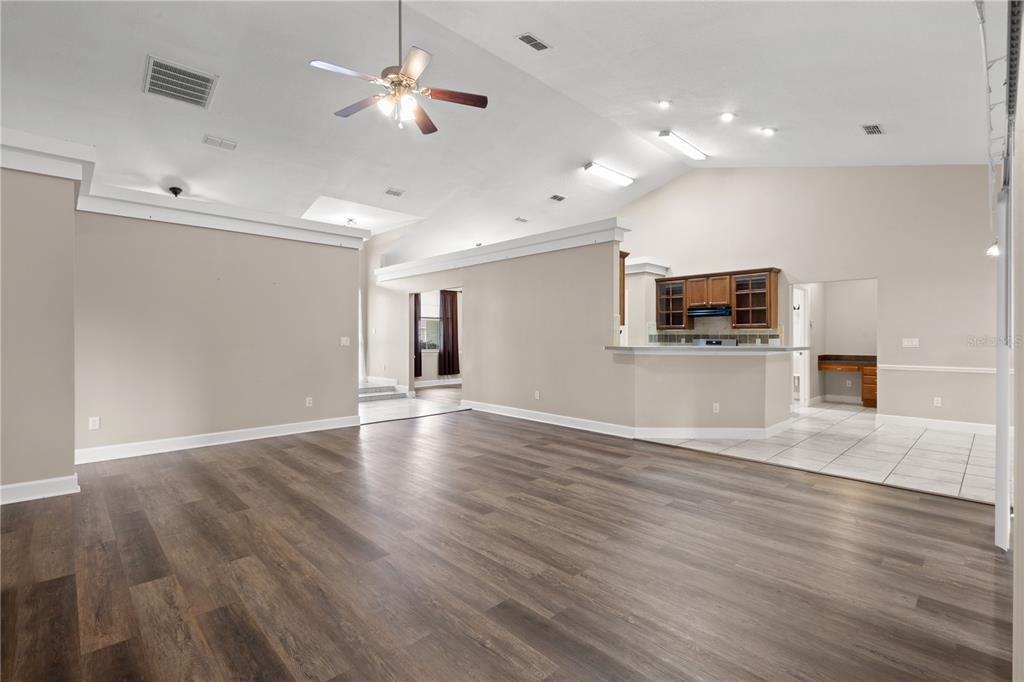 An open-concept living room with wood-look flooring, vaulted ceilings, and an adjacent kitchen area — 5320 SW 115TH LOOP, OCALA, FL