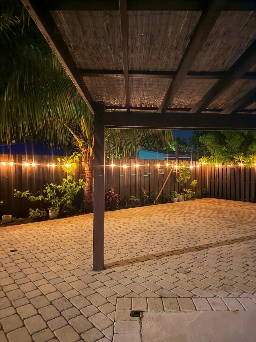 A paved patio at night features a wooden pergola and string lights along a fence — 2480 NE 13th Terrace, Pompano Beach FL 33064, POMPANO BEACH, FL