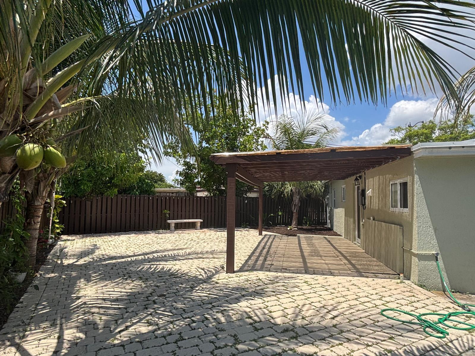 A backyard features a paved patio, a wooden pergola, a palm tree, and a fence — 2480 NE 13th Terrace, Pompano Beach FL 33064, POMPANO BEACH, FL