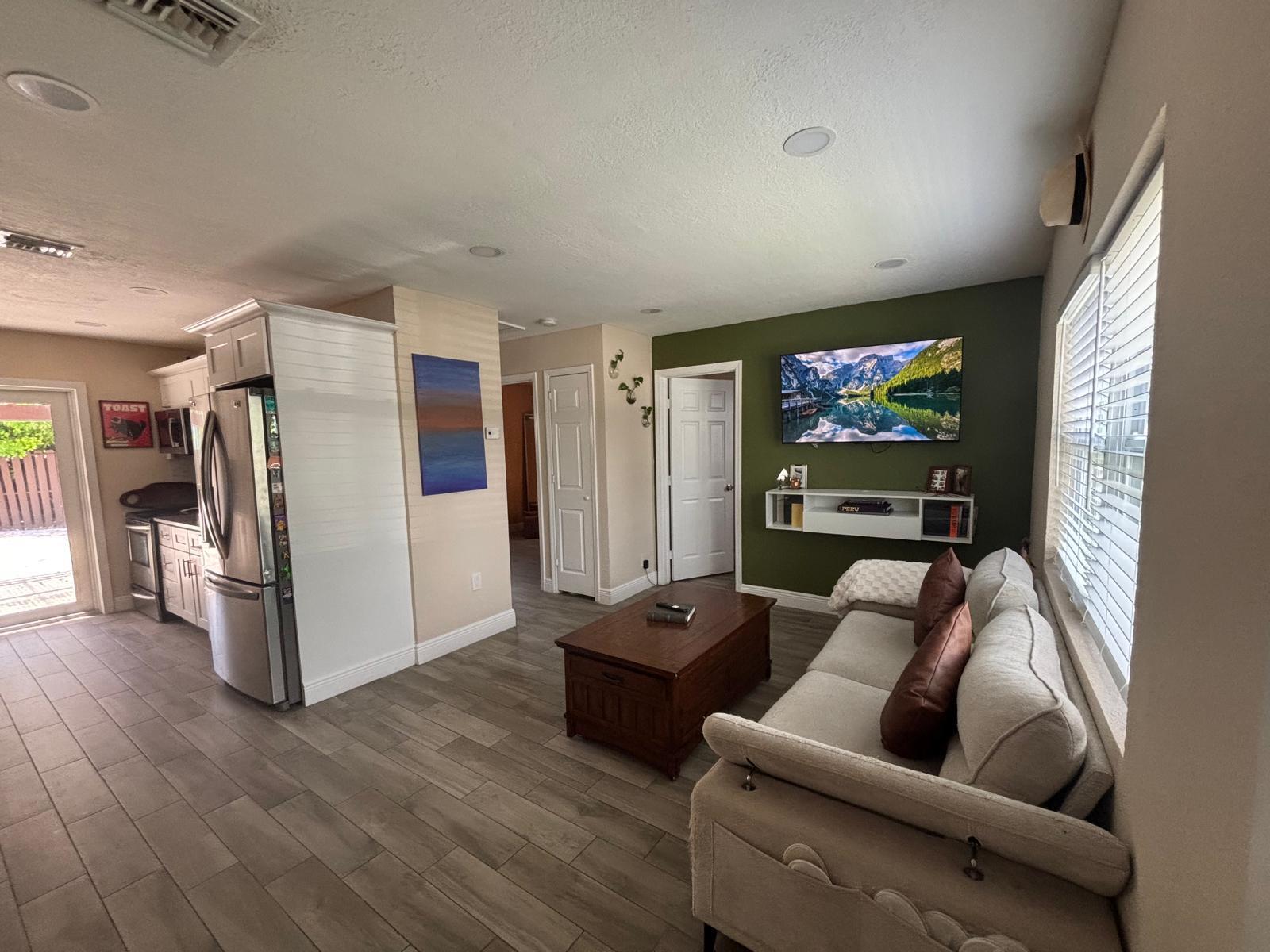 A living room with a green accent wall, wall-mounted television, and light wood-look tile flooring — 2480 NE 13th Terrace, Pompano Beach FL 33064, POMPANO BEACH, FL