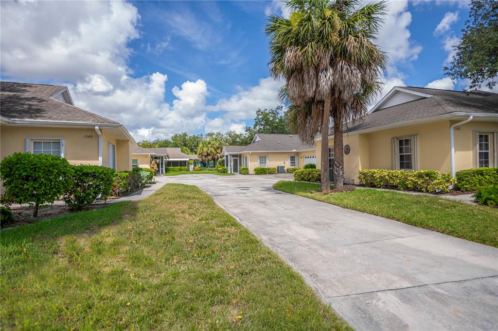 A concrete driveway leads between two yellow single-story residential buildings with palm trees — 1554 RED OAK LANE, PORT CHARLOTTE, FL