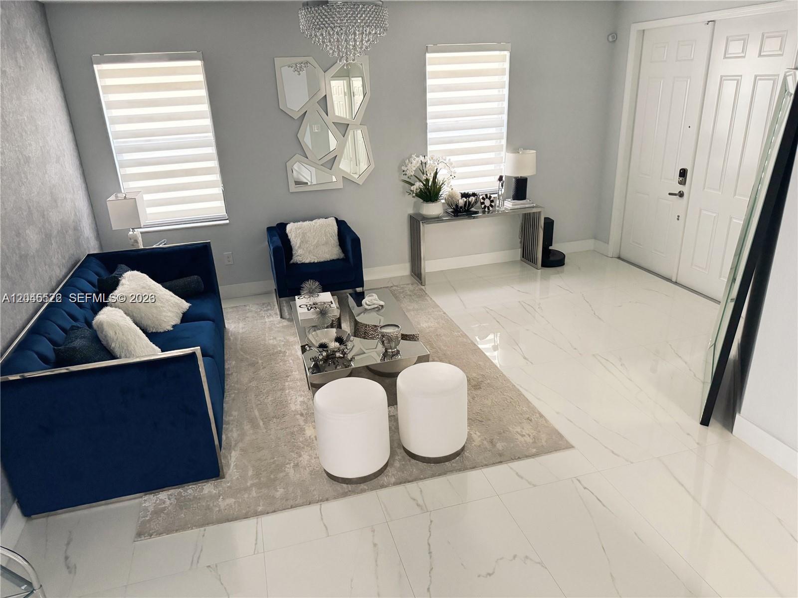 A modern living room features a blue velvet sofa, mirrored coffee table, and white tile floors — 8719 W 33rd Ave, Hialeah FL 33018, HIALEAH, FL