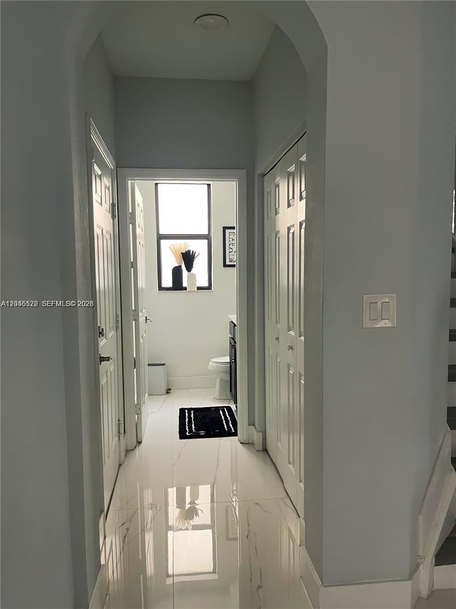 A hallway with white tile floors leads to a bathroom featuring a window and vanity — 8719 W 33rd Ave, Hialeah FL 33018, HIALEAH, FL