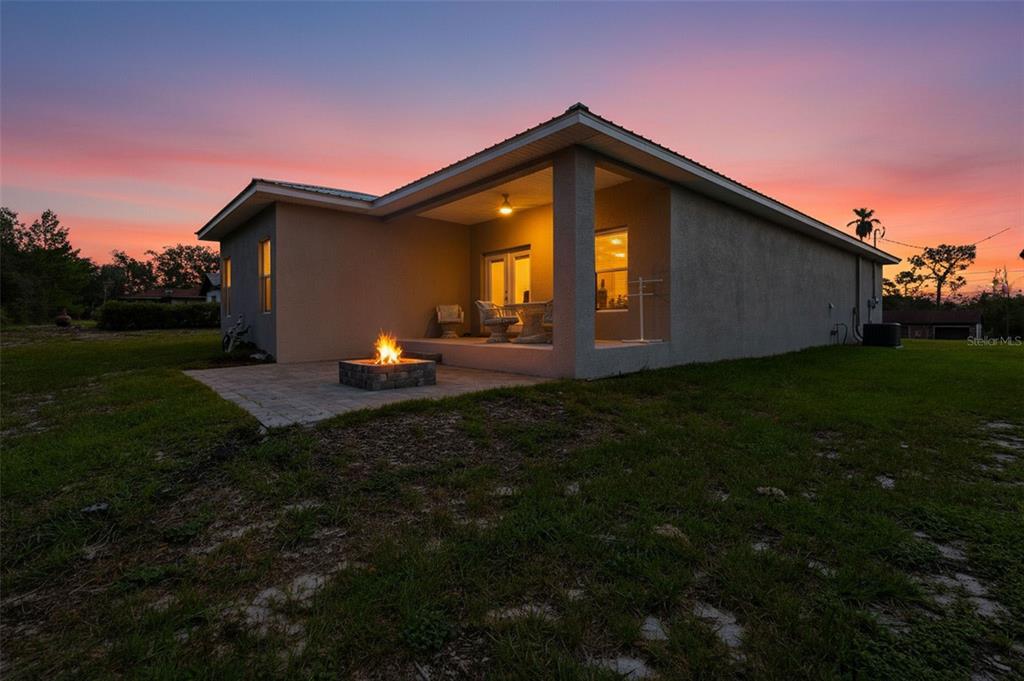 A house exterior at sunset features a covered patio with a fire pit on the lawn — 6454 FREEPORT DRIVE, SPRING HILL, FL