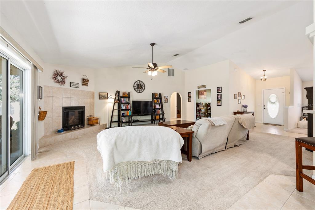 A living room features a tiled fireplace, carpeted flooring, a ceiling fan, and an entryway — 4515 NW 6TH CIRCLE, OCALA, FL