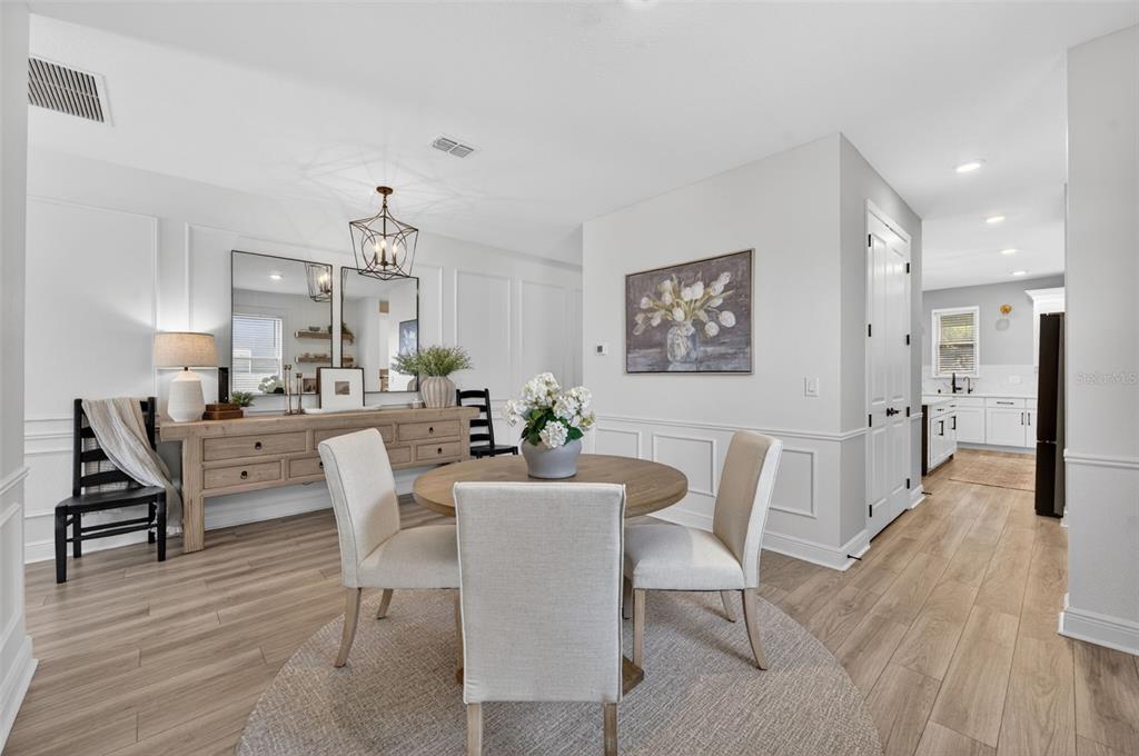 A dining area features a round wooden table, upholstered chairs, and a sideboard with mirrors — 1112 PEARL TREE ROAD, DELTONA, FL