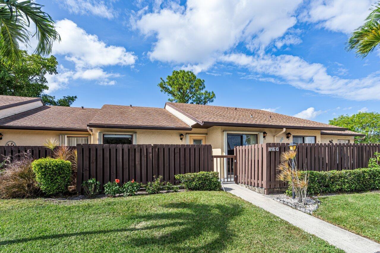 A single-story tan house features a brown wooden privacy fence and a concrete walkway — 816 Sky Pine Way # G, FL 33415, FL