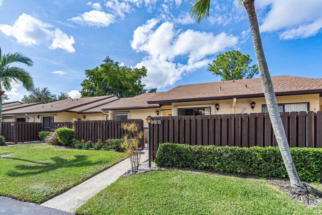 A single-story residential unit features a brown wooden fence, a walkway, and a palm tree — 816 Sky Pine Way # G, FL 33415, FL