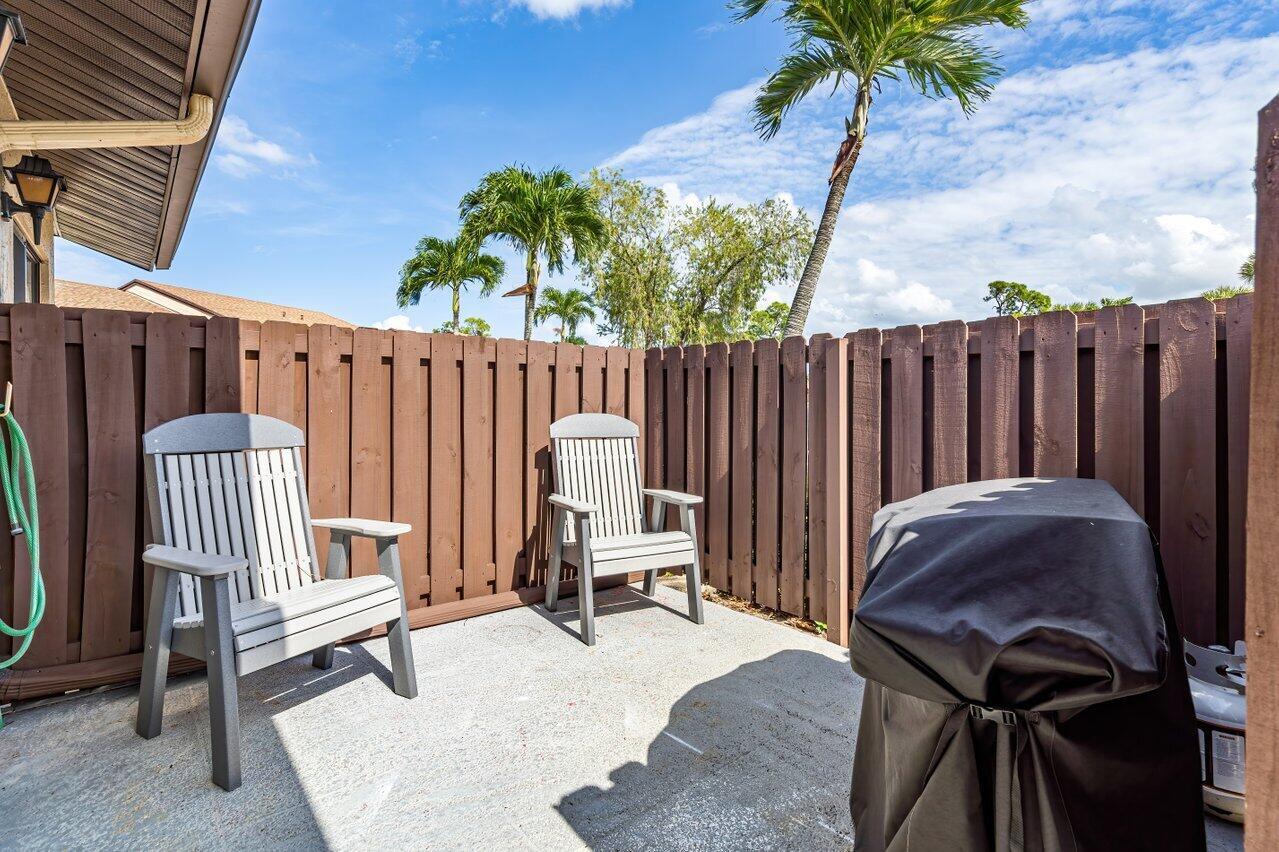 A concrete patio features two wooden chairs, a covered grill, and a wooden privacy fence — 816 Sky Pine Way # G, FL 33415, FL