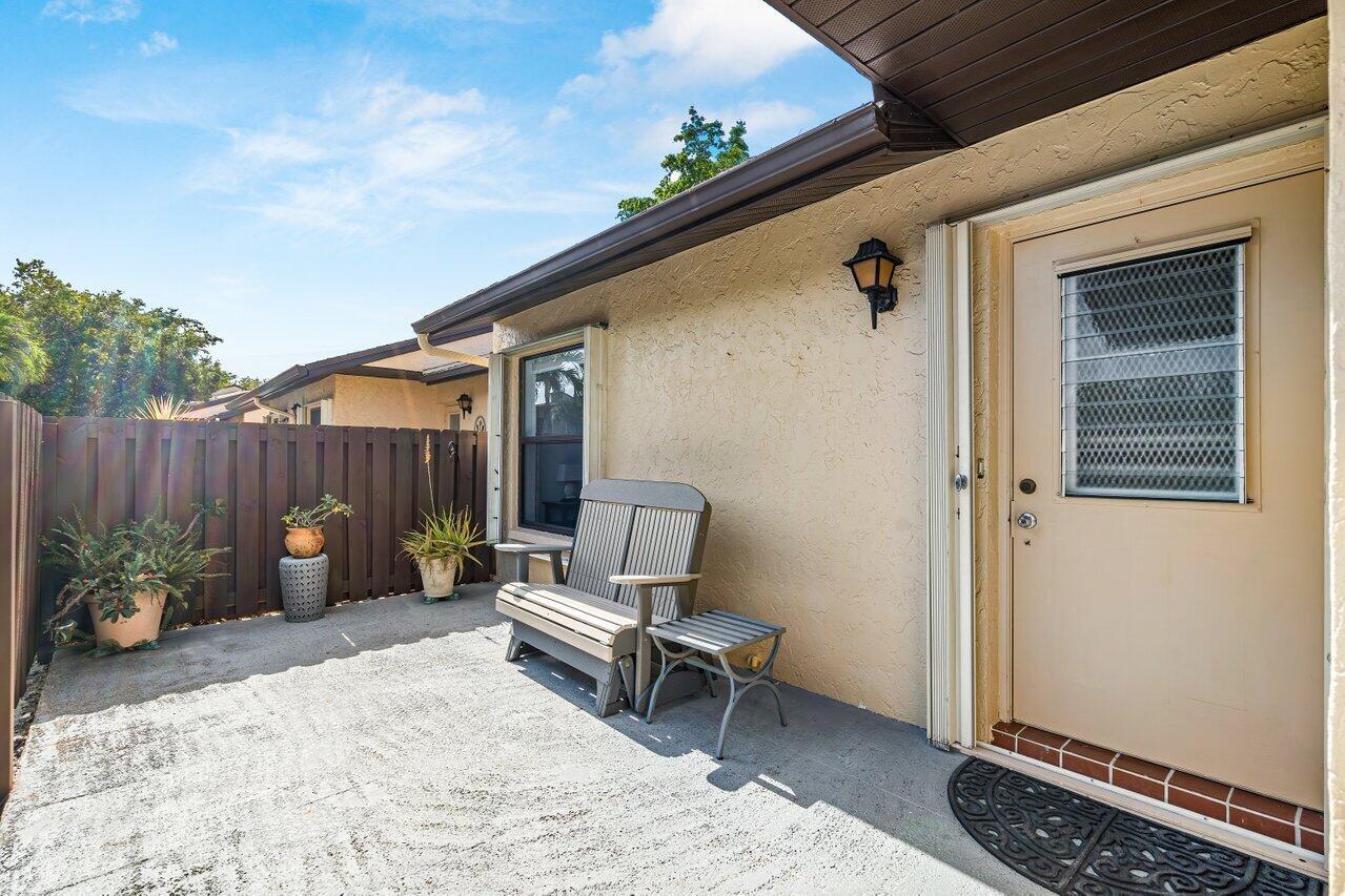 A concrete patio features a wooden bench, a small side table, and a tan exterior door — 816 Sky Pine Way # G, FL 33415, FL