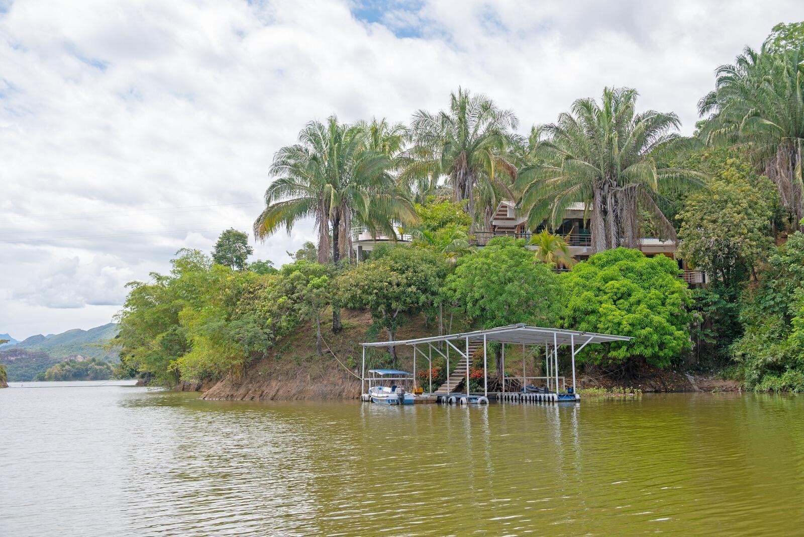 A house sits on a lush, tree-covered hill above a lake with a private boat dock — El Paraiso Del Lago, FL