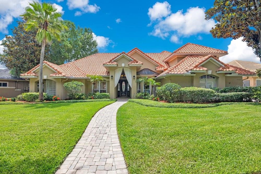 A single-story house with a tiled roof, arched entryway, and a stone walkway across grass — 7718 DEBEAUBIEN DRIVE, ORLANDO, FL