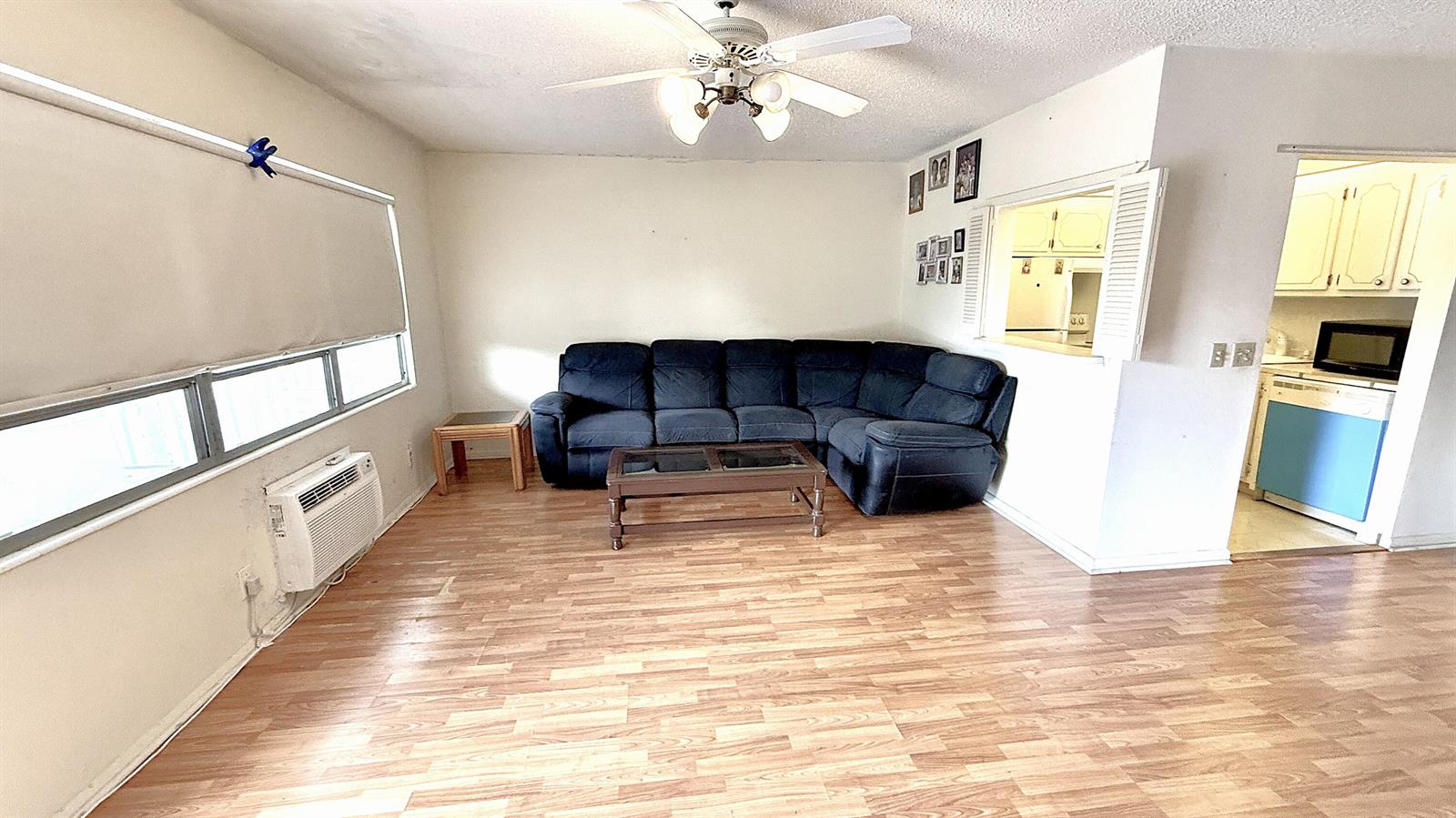 A living room features wood-look flooring, a dark sectional sofa, and an open kitchen pass-through — 122 Oakridge I, Deerfield Beach FL 33442, DEERFIELD BEACH, FL
