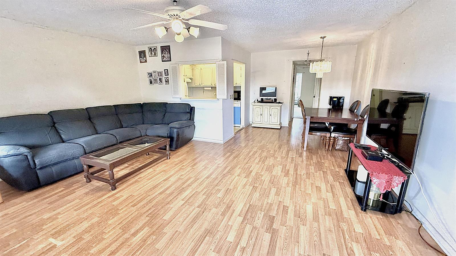 A living and dining area features wood-look flooring, a dark sectional sofa, and a television — 122 Oakridge I, Deerfield Beach FL 33442, DEERFIELD BEACH, FL