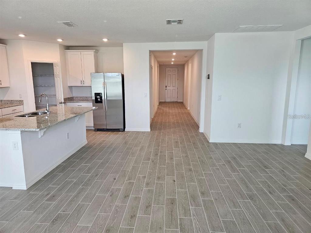 A kitchen with a granite island and stainless steel refrigerator opens to a hallway — 5309 MADDIE DRIVE, HAINES CITY, FL