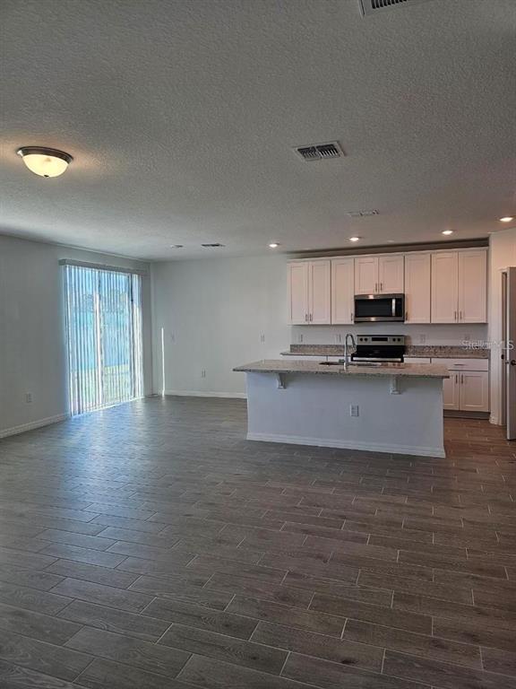An open-concept kitchen with white cabinets and a center island overlooks a living area — 5309 MADDIE DRIVE, HAINES CITY, FL