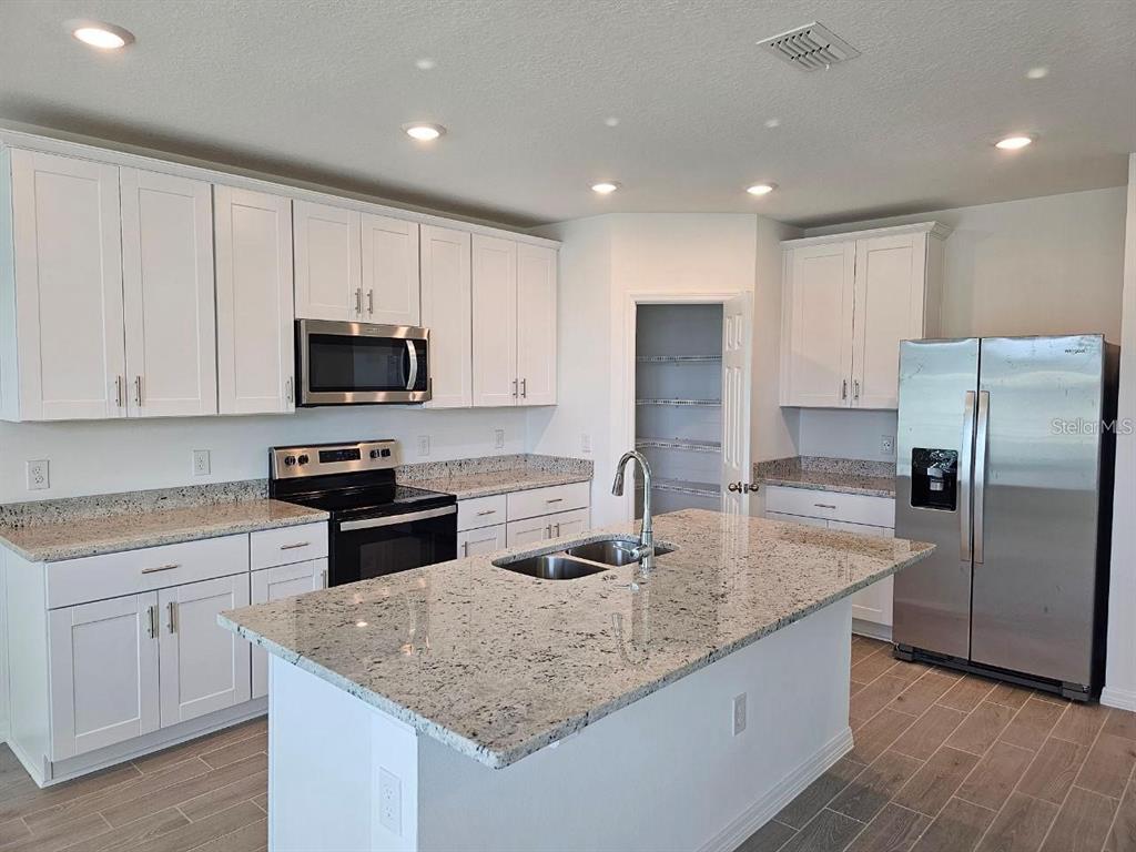A kitchen features white cabinets, granite countertops, a center island, and stainless steel appliances — 5309 MADDIE DRIVE, HAINES CITY, FL