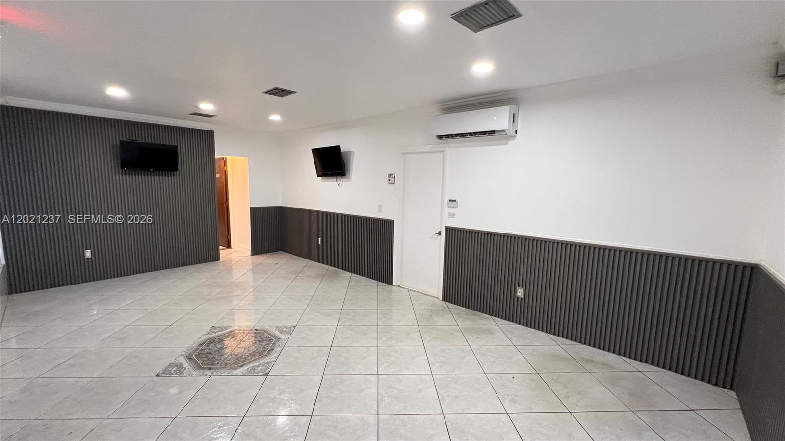 A room with white walls, gray vertical-slat wainscoting, tiled floors, and two wall-mounted televisions — 2727 NW 34th St, Miami FL 33142, MIAMI, FL