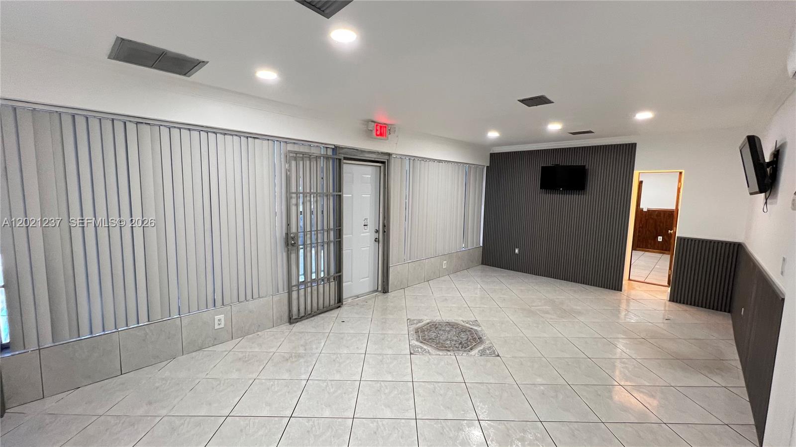 A room with white tile floors, vertical blinds, a security gate, and a dark accent wall — 2727 NW 34th St, Miami FL 33142, MIAMI, FL