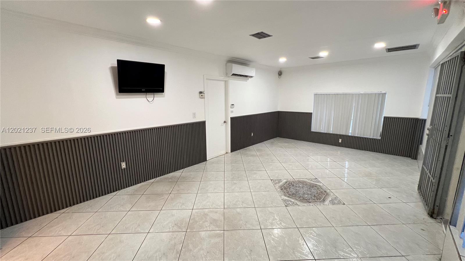A room with light-colored tile floors, dark vertical wall paneling, and a wall-mounted television — 2727 NW 34th St, Miami FL 33142, MIAMI, FL