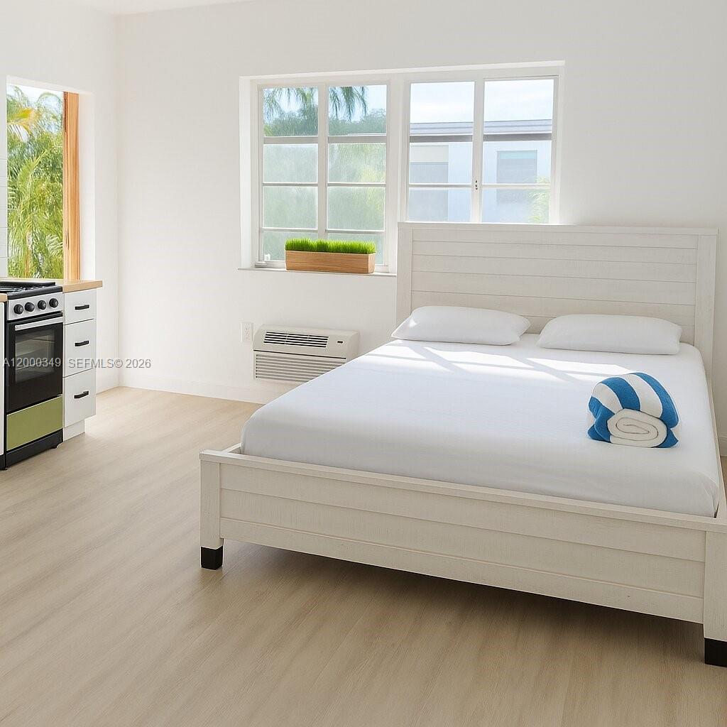 A bedroom with a white bed frame, light wood flooring, and an adjacent kitchen area — 301 86th St # 4A, Miami Beach FL 33141, MIAMI BEACH, FL