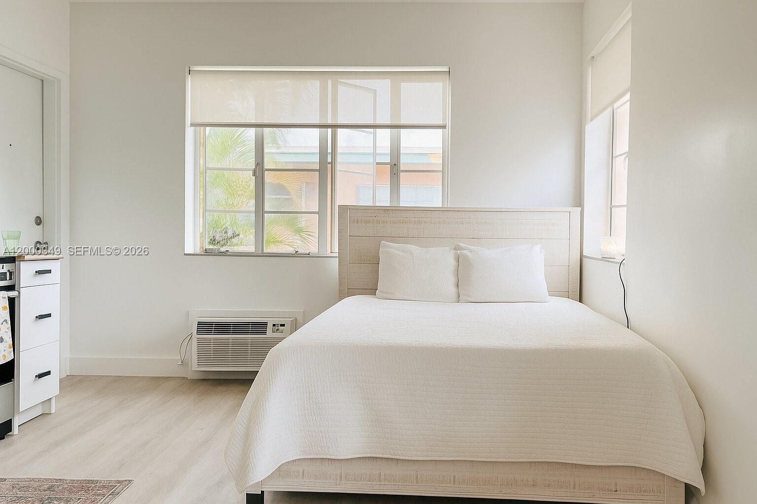 A bedroom features a white bed, a window air conditioning unit, and light wood flooring — 301 86th St # 4A, Miami Beach FL 33141, MIAMI BEACH, FL