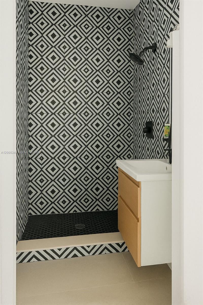 A bathroom features a walk-in shower with geometric patterned tile and a wooden vanity — 301 86th St # 4A, Miami Beach FL 33141, MIAMI BEACH, FL