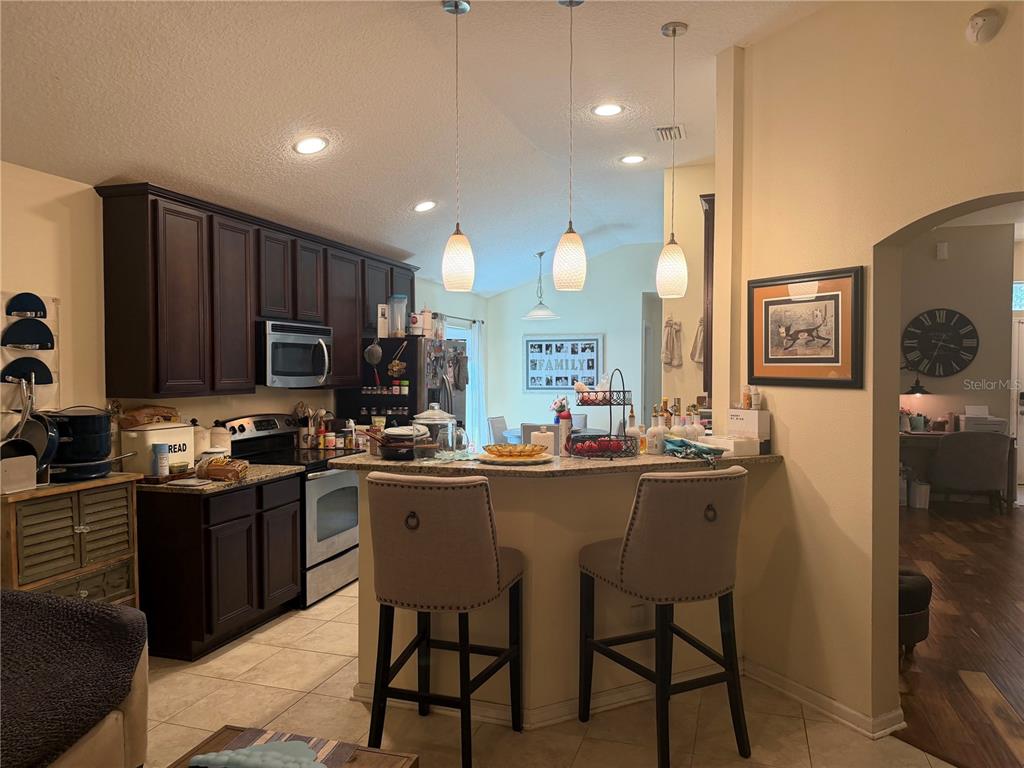 A kitchen features dark wood cabinets, granite countertops, a breakfast bar, and three pendant lights — 4851 NW 81ST AVENUE, GAINESVILLE, FL