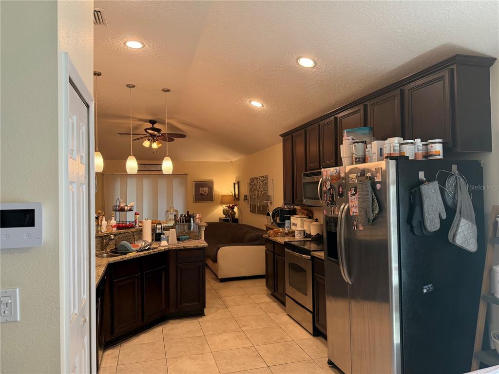 A kitchen with dark wood cabinets, stainless steel appliances, and tile flooring opens to a living area — 4851 NW 81ST AVENUE, GAINESVILLE, FL
