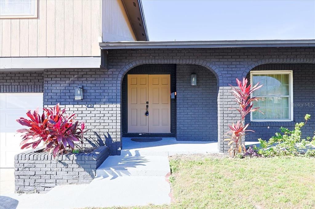 A dark brick exterior features an arched entryway with double tan doors and landscaping — 2244 MENOMONEE COURT, ORLANDO, FL