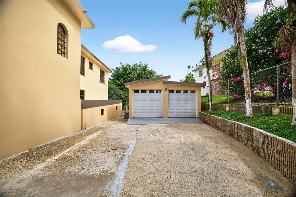 A concrete driveway leads to a two-car garage next to a tan multi-story house — PR-184 KM 32.4 S BEATRIZ, CAYEY, PR