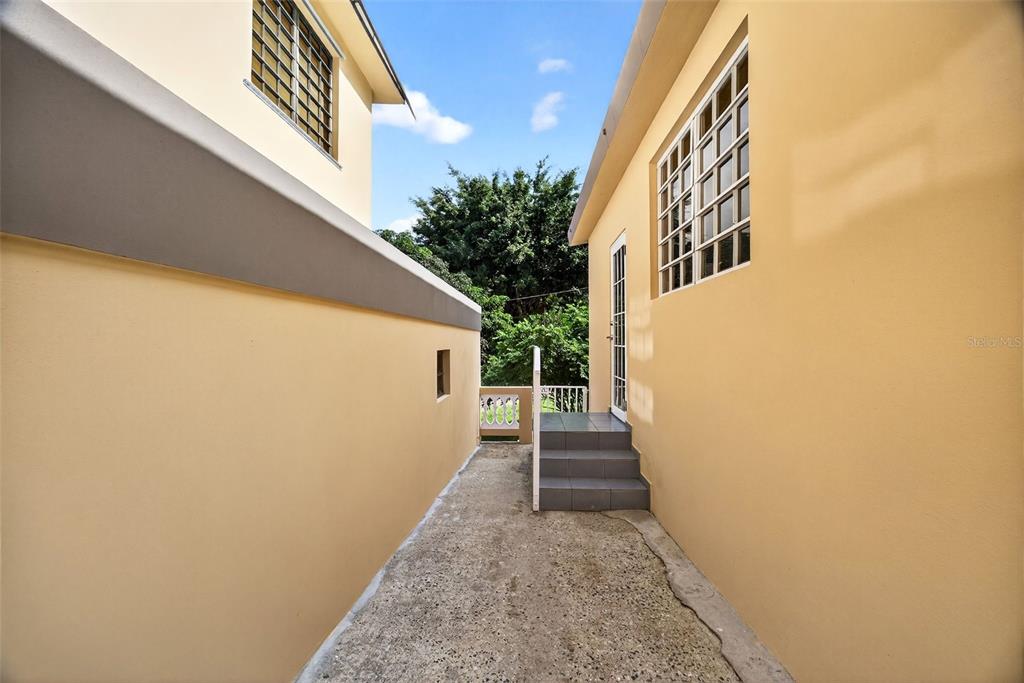 A concrete walkway leads between two yellow exterior walls toward a set of stairs — PR-184 KM 32.4 S BEATRIZ, CAYEY, PR