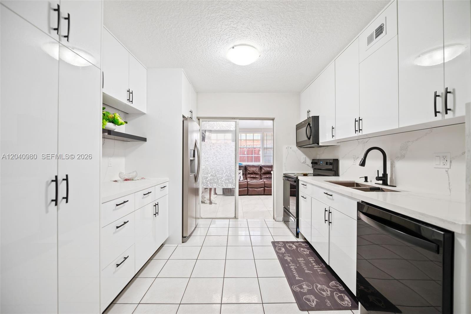 A galley kitchen features white cabinets, stainless steel appliances, and white tiled flooring — 7817 W 36th Ave # 101, Hialeah FL 33018, HIALEAH, FL