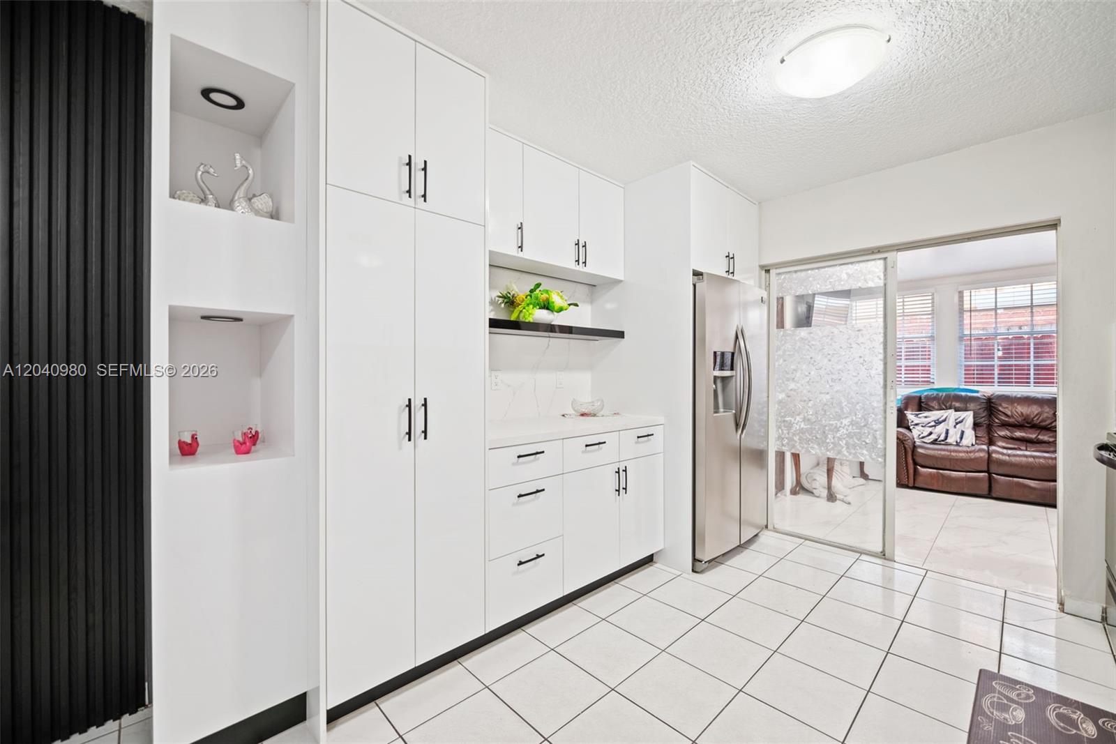 A modern kitchen features white cabinetry, stainless steel appliances, and white tiled flooring — 7817 W 36th Ave # 101, Hialeah FL 33018, HIALEAH, FL