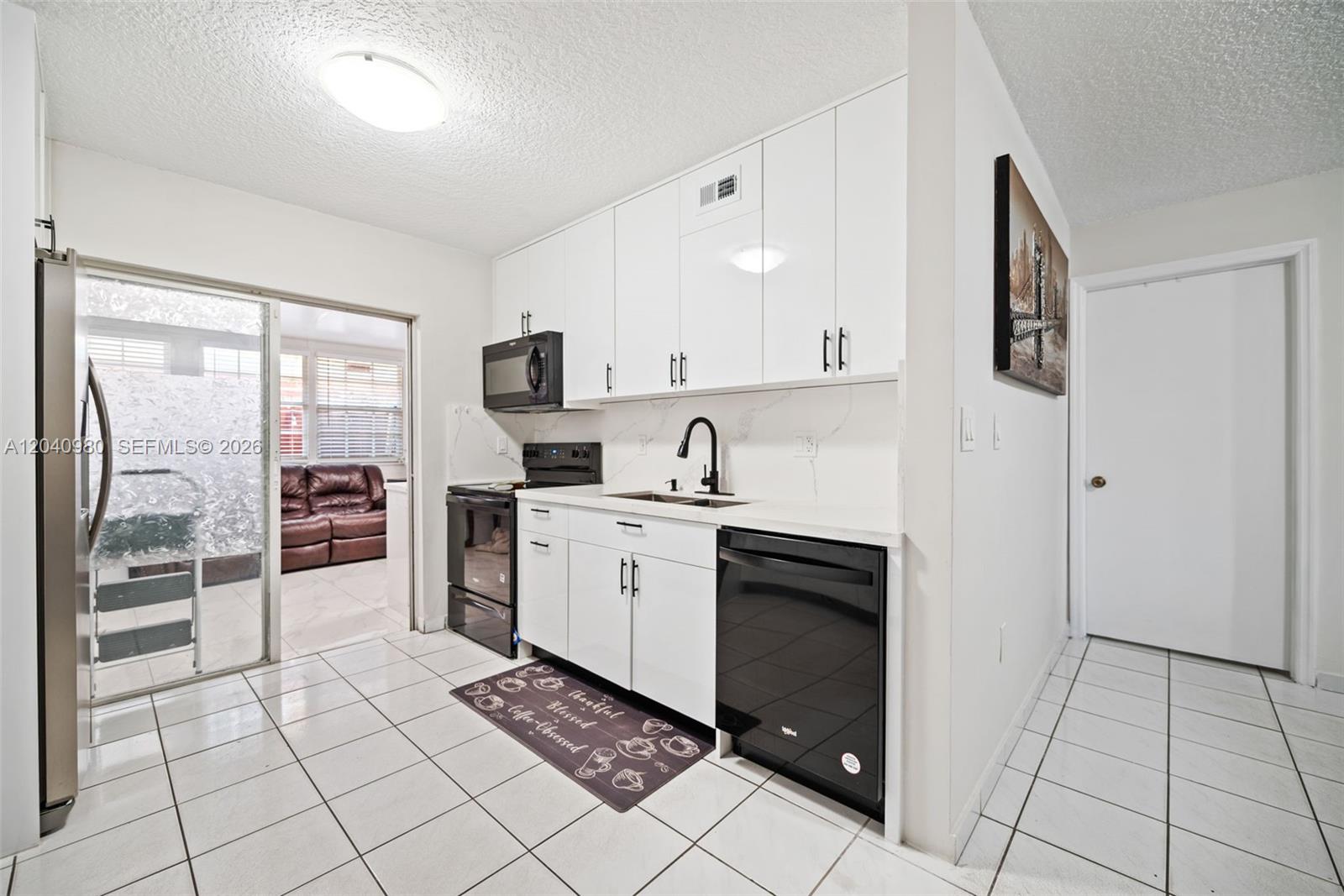 A kitchen features white cabinets, black appliances, and white tiled flooring — 7817 W 36th Ave # 101, Hialeah FL 33018, HIALEAH, FL