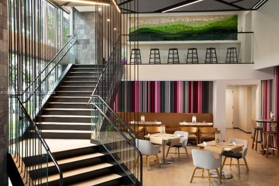 A modern interior features a prominent staircase with metal railings leading to a mezzanine dining area — 227 NE 2nd St # 1707, Miami FL 33132, MIAMI, FL