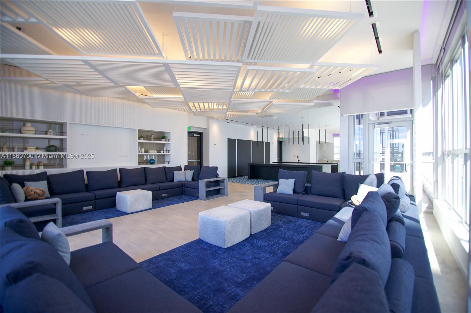 A modern lounge area features blue sectional sofas, white ottomans, and a geometric slatted ceiling — 227 NE 2nd St # 1707, Miami FL 33132, MIAMI, FL