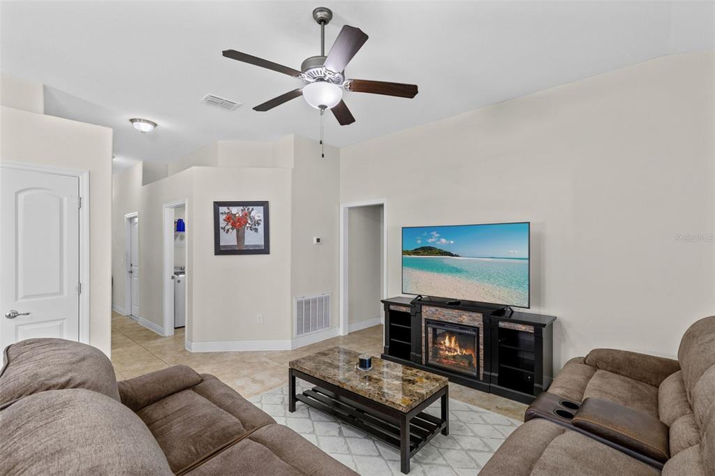 A living room features a ceiling fan, a fireplace console with a television, and tile flooring — 399 BUCHANNAN DRIVE, DAVENPORT, FL