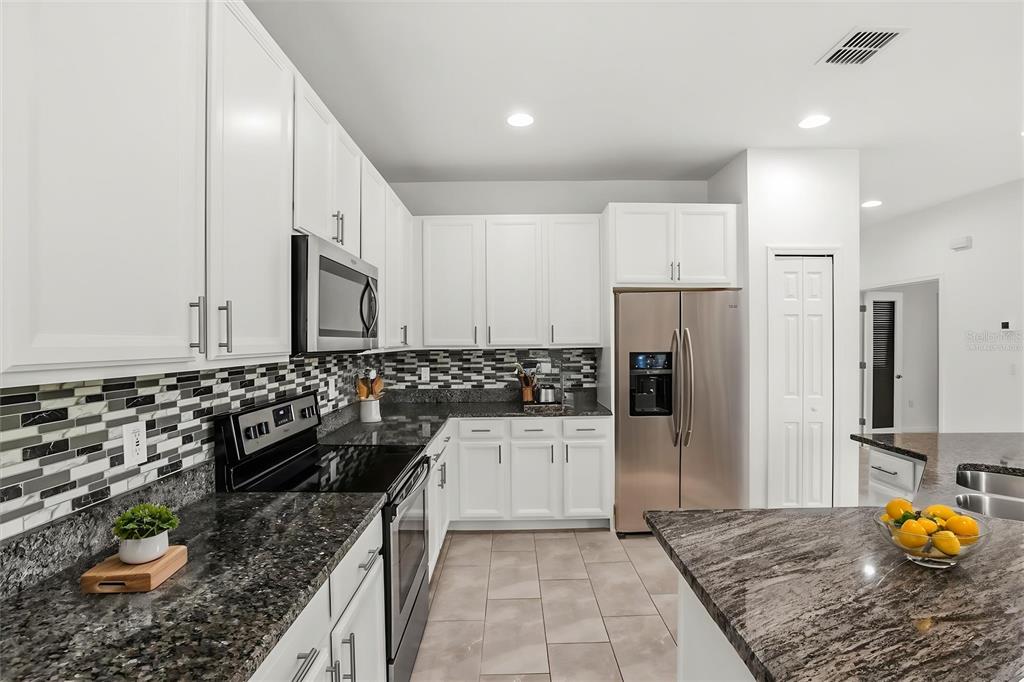 A kitchen features white cabinets, dark granite countertops, a mosaic tile backsplash, and stainless appliances — 3788 SALTMARSH LOOP, SANFORD, FL