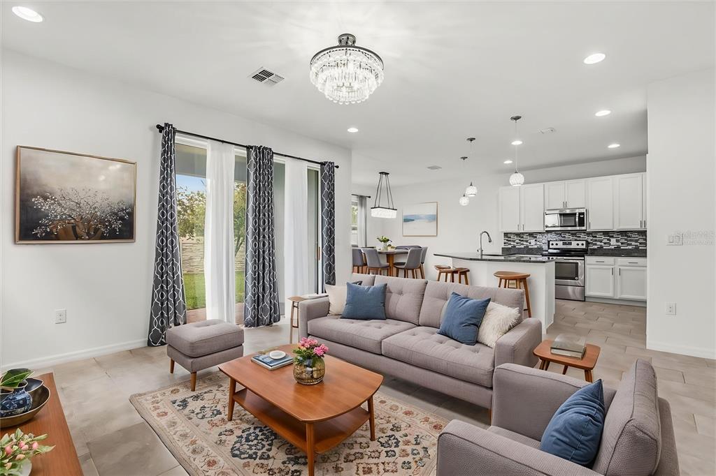 A bright open-concept living room features a grey sofa, coffee table, and adjacent kitchen area — 3788 SALTMARSH LOOP, SANFORD, FL