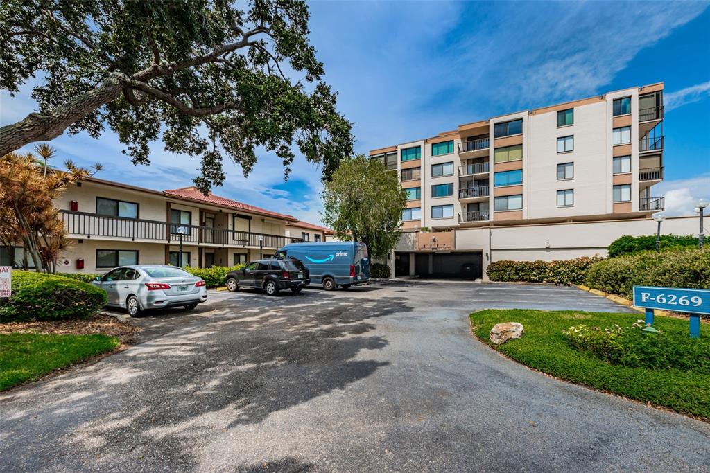 An exterior view shows a parking lot in front of a multi-story apartment building — 6269 PALMA DEL MAR BOULEVARD S UNIT 105, ST PETERSBURG, FL