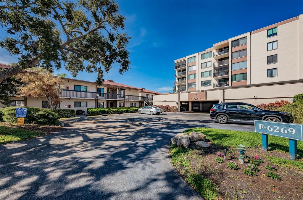 An exterior view of a multi-story apartment complex with a parking lot and trees — 6269 PALMA DEL MAR BOULEVARD S UNIT 105, ST PETERSBURG, FL
